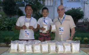 Trois membres de l’équipe Light of Hope, dont un enfant, présentent des sachets de riz destinés à la distribution humanitaire aux Philippines.