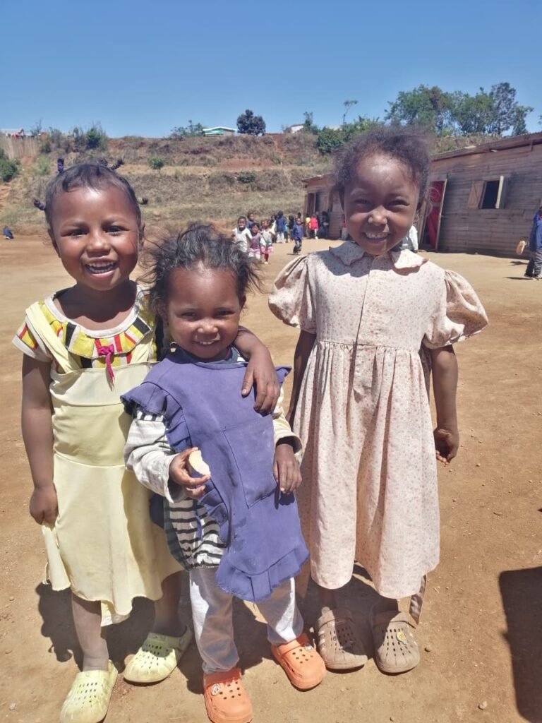 Tre bambine malgasce sorridenti davanti alla scuola sostenuta da Helping Hands ad Antsirabé